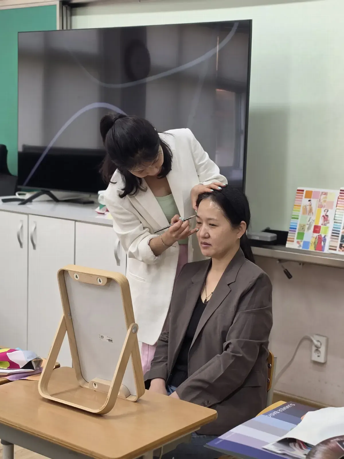 퍼스널컬러 출장 컨설팅에서 거울 앞에 앉은 참가자의 얼굴빛을 확인하는 컨설턴트